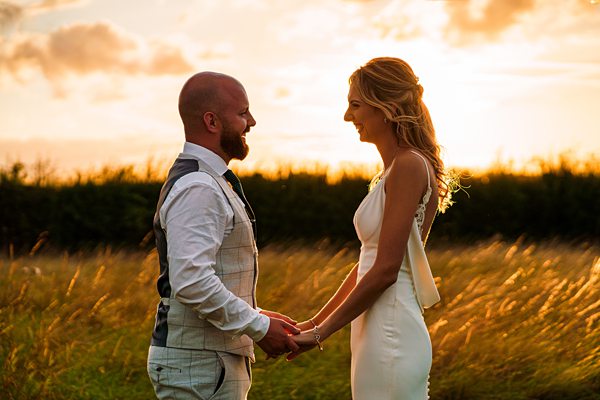 Couple holding hands in sunset field.