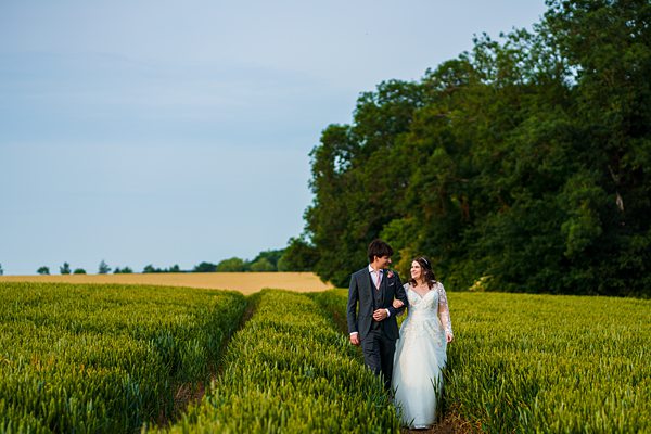 Bride and groom walking in a wheat field.