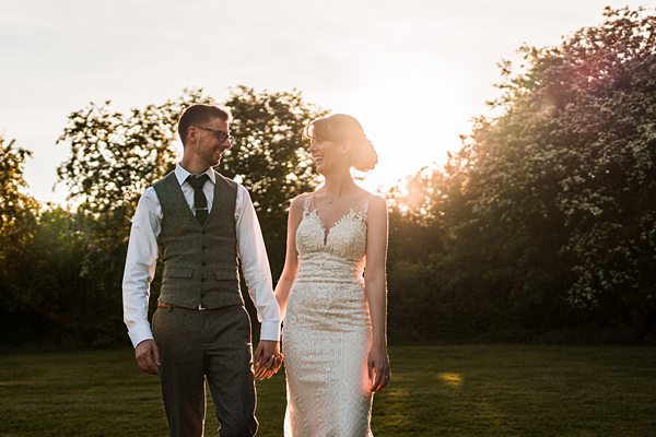 Bride and groom holding hands outdoors at sunset.