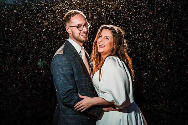 Smiling couple in wedding attire under sparkling lights.