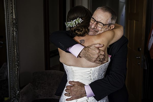 Bride embraces elderly man warmly, emotional moment.