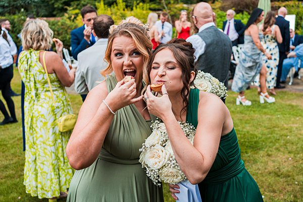 Two women enjoy wedding cupcakes, surrounded by guests.