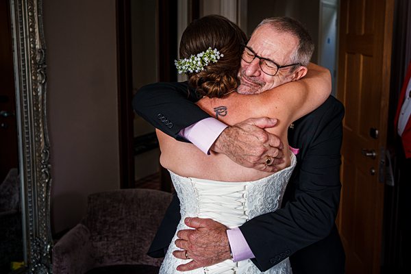 Bride hugs older man warmly indoors.