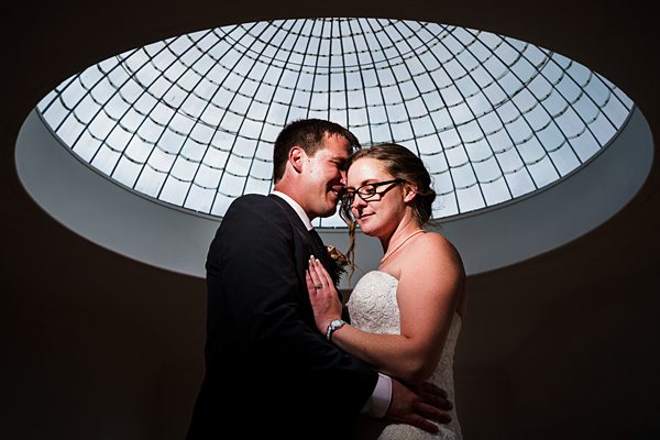 Bride and groom embracing under domed ceiling.