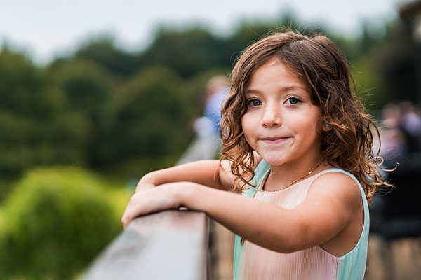 Smiling child outdoors, leaning on wooden railing.