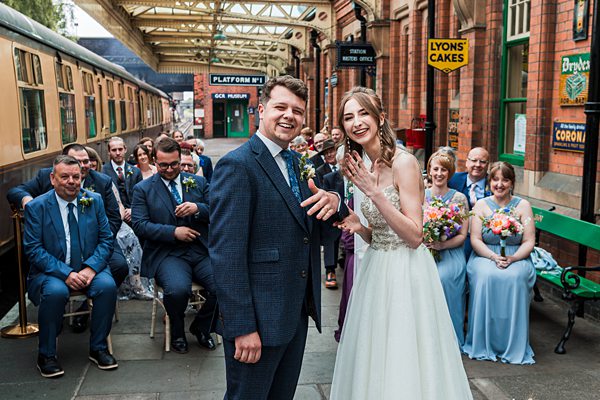 Couple marries at vintage railway station, guests seated.