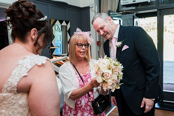 Smiling guests admire wedding bouquet indoors.