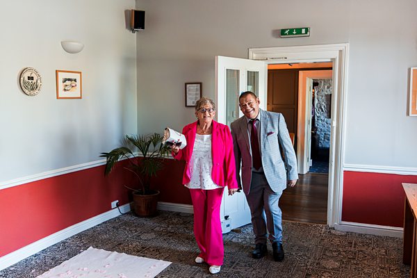 Elderly couple entering room, woman in pink suit.
