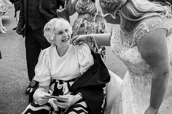 Bride greets elderly woman in wheelchair at wedding.