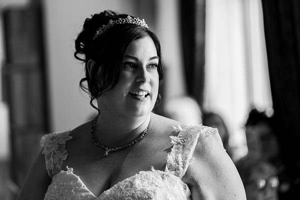 Bride in lace gown smiling indoors, black and white.