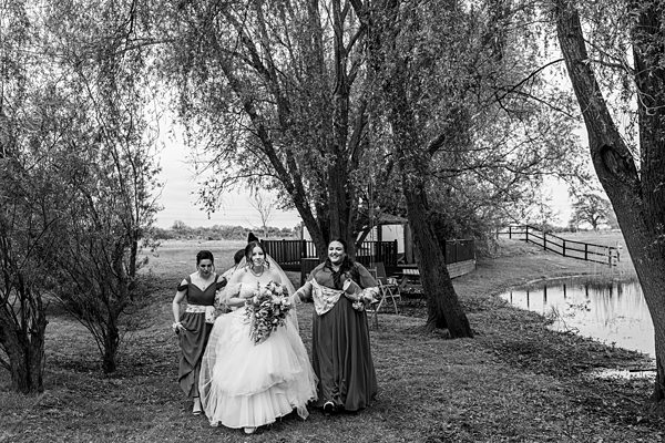Bride walks with bridesmaids through a park.