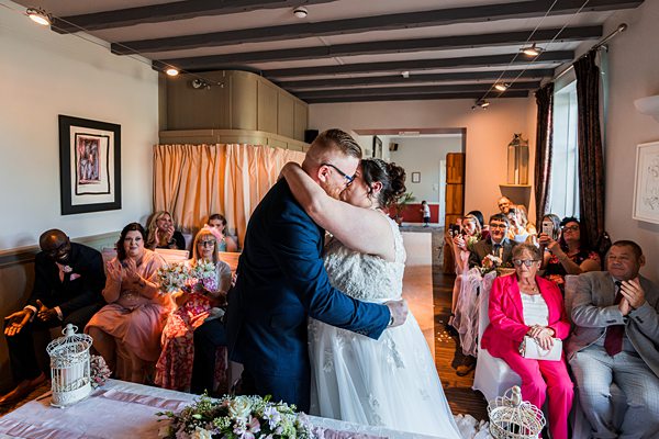 Bride and groom kiss at indoor ceremony.