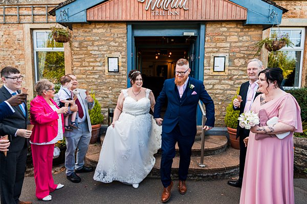Wedding couple exits venue with family celebrating.
