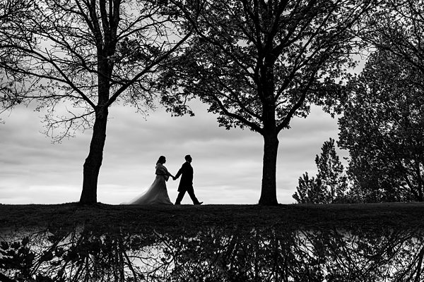 Silhouetted couple walking under trees by a lake.