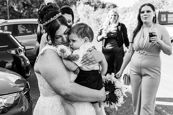 Bride embraces child, surrounded by guests, black and white
