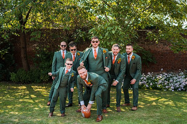 Groomsmen in suits posing with football outdoors.