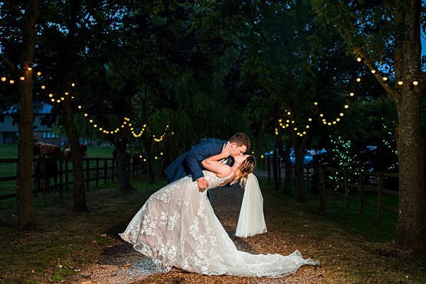 Couple kissing under trees with string lights.