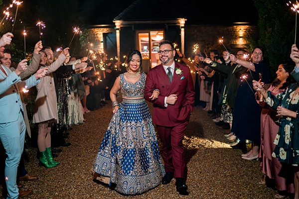 Couple walking through guests with sparklers at night.