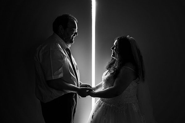 Couple holding hands, silhouetted against bright light.
