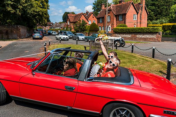 Women in red convertible car celebrating with flowers.
