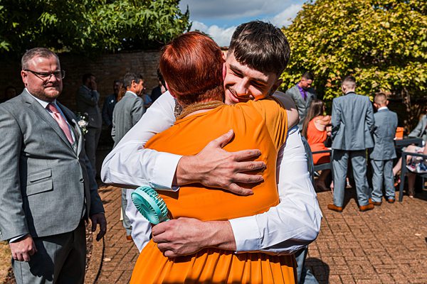 Two people hugging at outdoor event with guests.