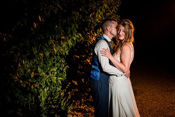Couple embracing under night sky beside green foliage.