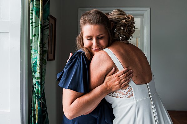 Two women embracing happily indoors, one in wedding dress.