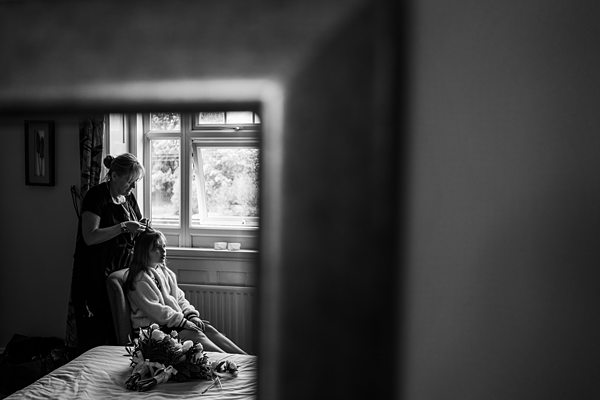 Woman styling hair, bride sitting, reflected in mirror.