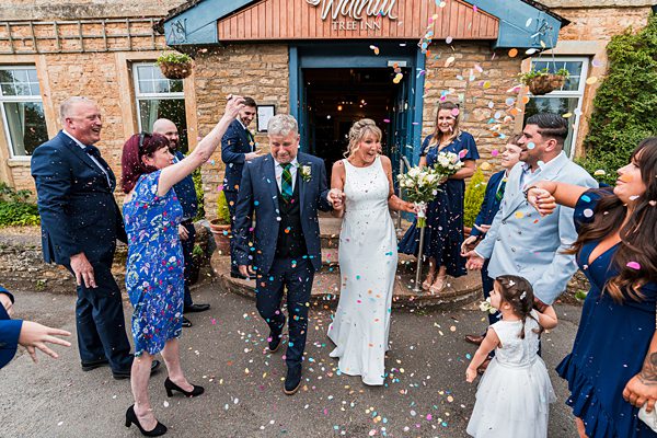 Wedding celebration with guests throwing confetti outdoors.