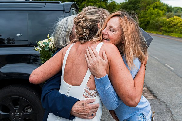 Three women hugging by a car, showing joy.