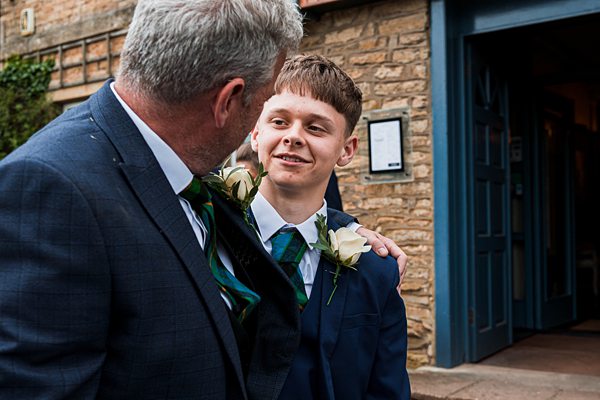 Father and son at wedding, smiling in suits.