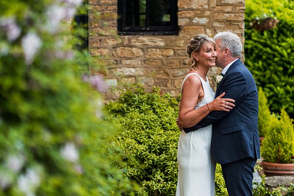 Couple embracing in garden near stone cottage.