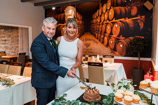 Couple cutting wedding cake in restaurant setting.