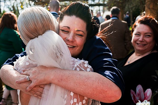 Wedding guests hugging outdoors under the sun.