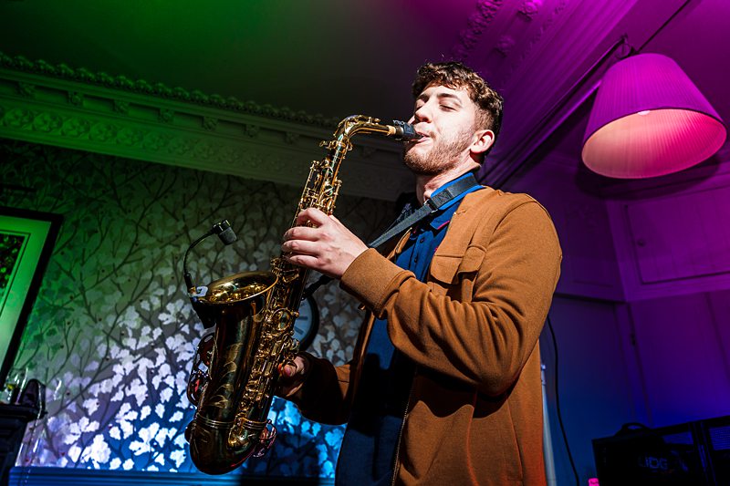 Man plays saxophone in colourful room