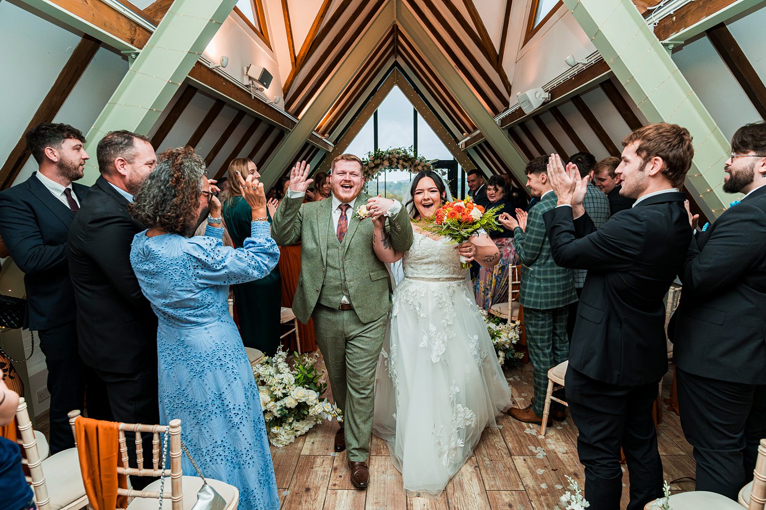 Newlyweds celebrate surrounded by clapping guests indoors.