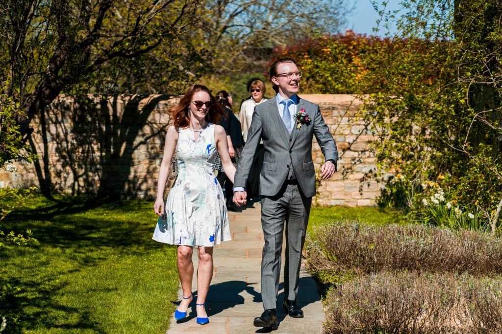 Couple walking in garden path, holding hands, laughing.