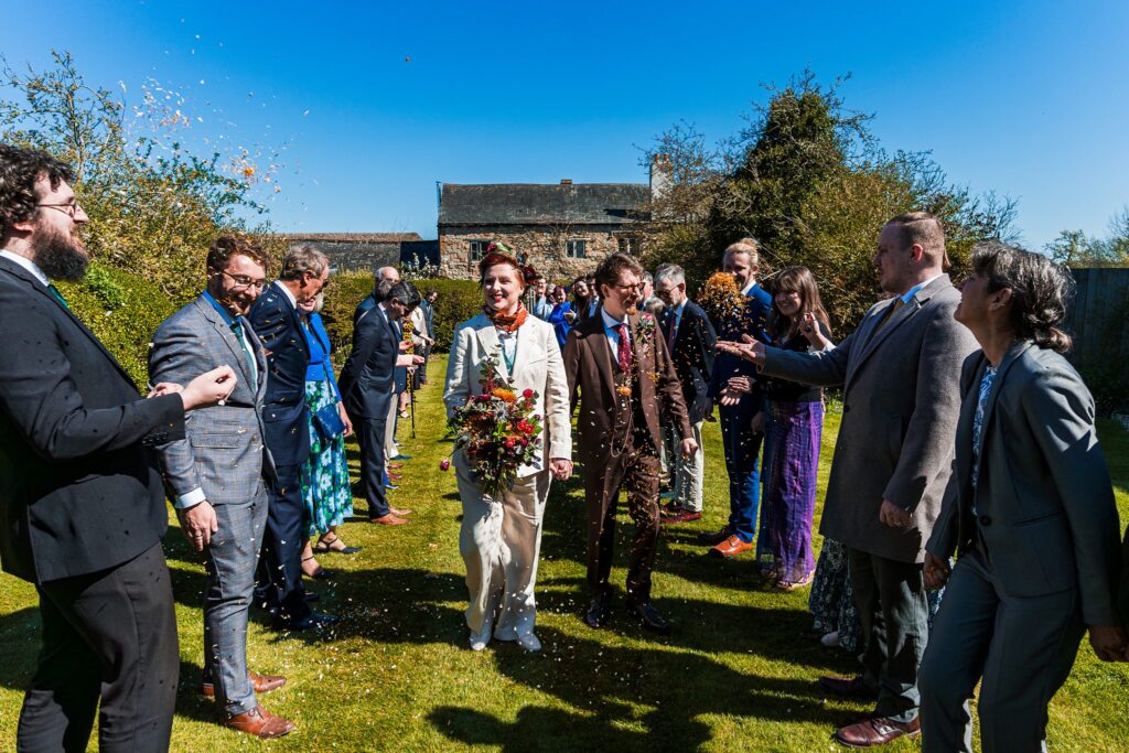 Wedding couple walks through confetti and cheering guests.