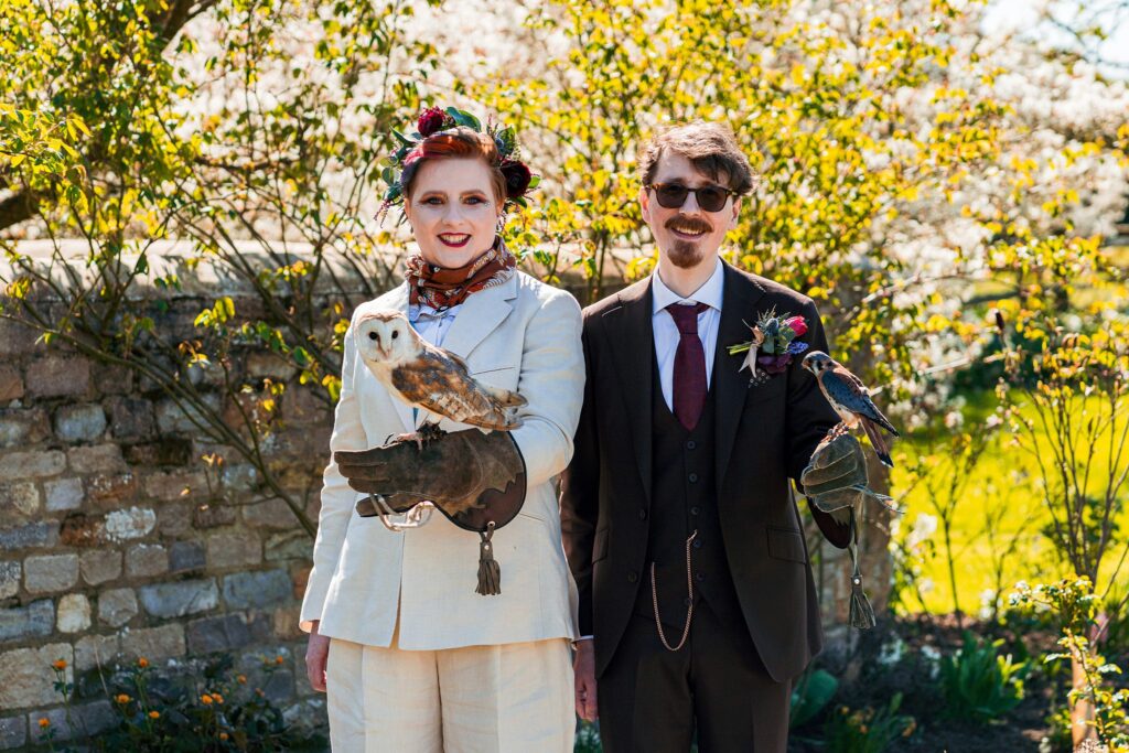 Couple dressed with birds on arms, outdoor setting.