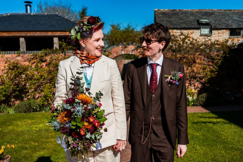 Smiling couple holding hands outdoors, colourful bouquet.