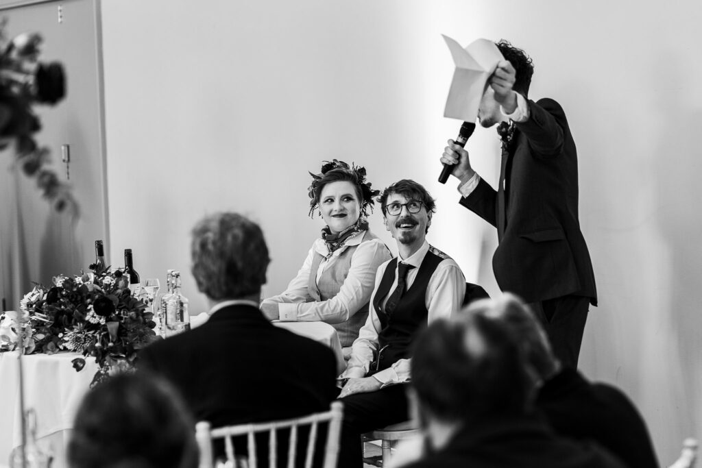Wedding speech with bride and groom seated, smiling.
