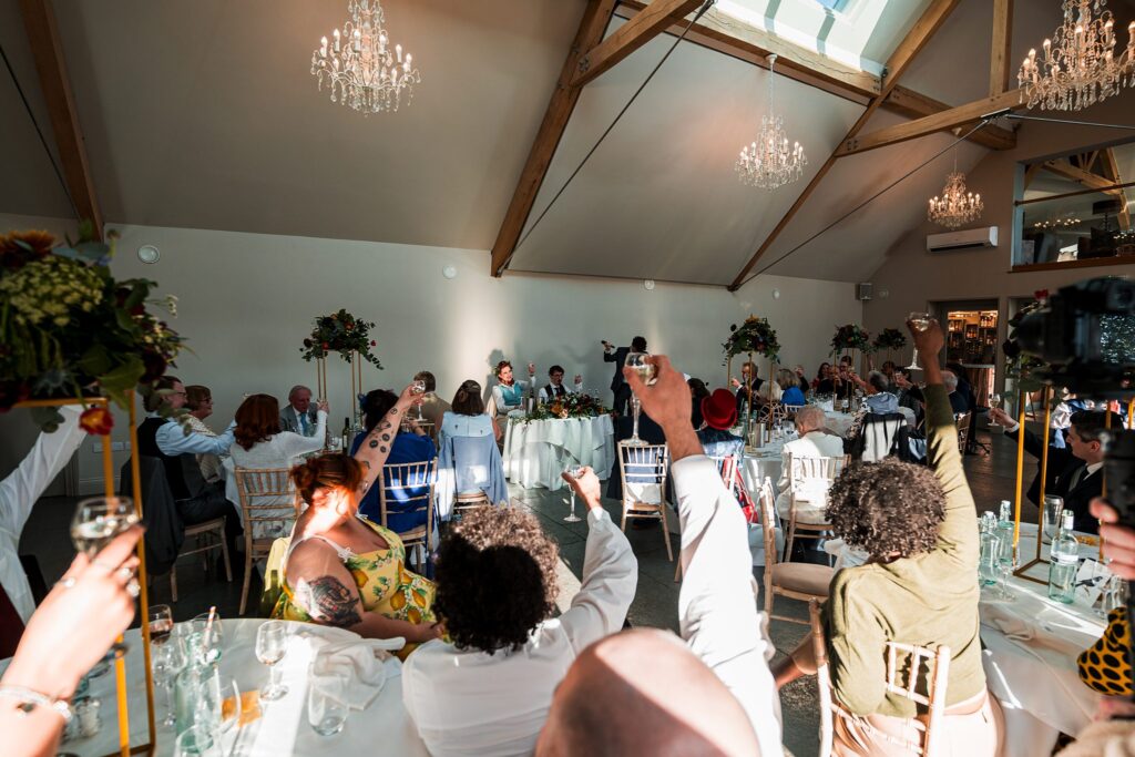 Guests raising glasses at a wedding reception toast.