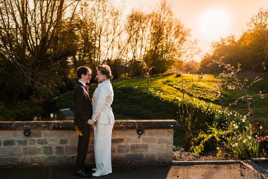 Couple holding hands on a sunny countryside bridge.