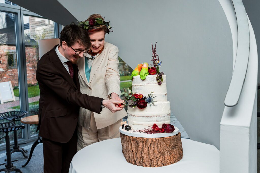 Couple cutting rustic wedding cake together indoors.