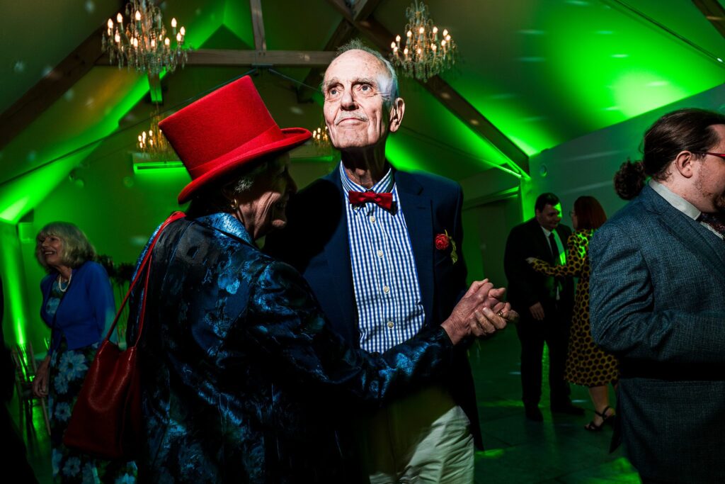 Elderly couple dancing at a party with green lights.
