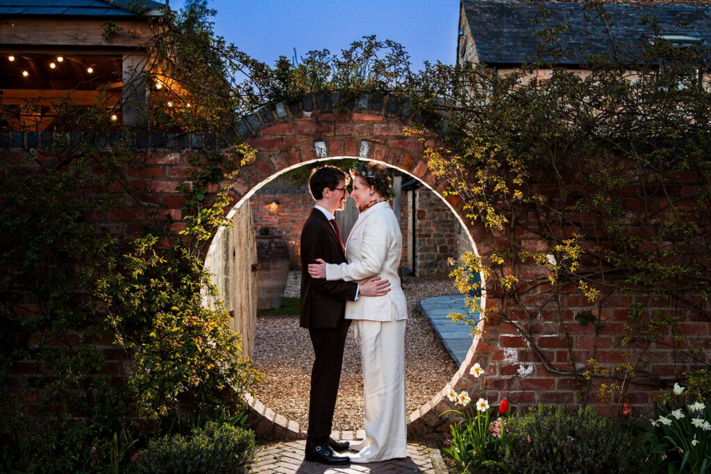 Couple embracing under brick garden archway.