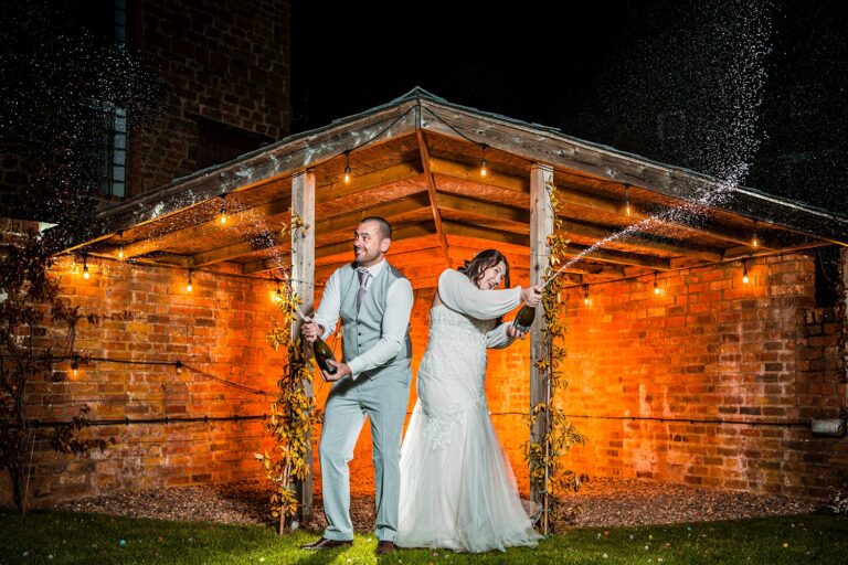 Couple celebrate with champagne under rustic shelter.