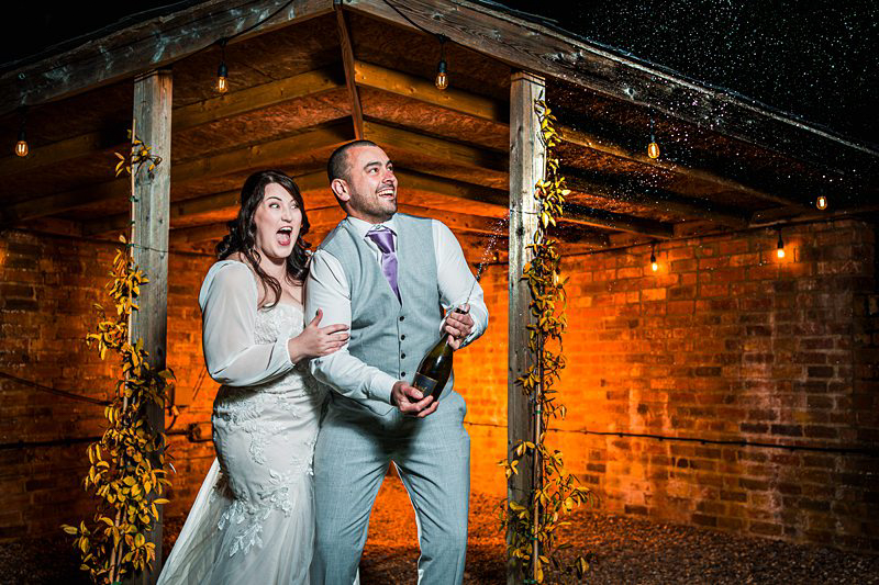 Couple celebrating with champagne at rustic venue.