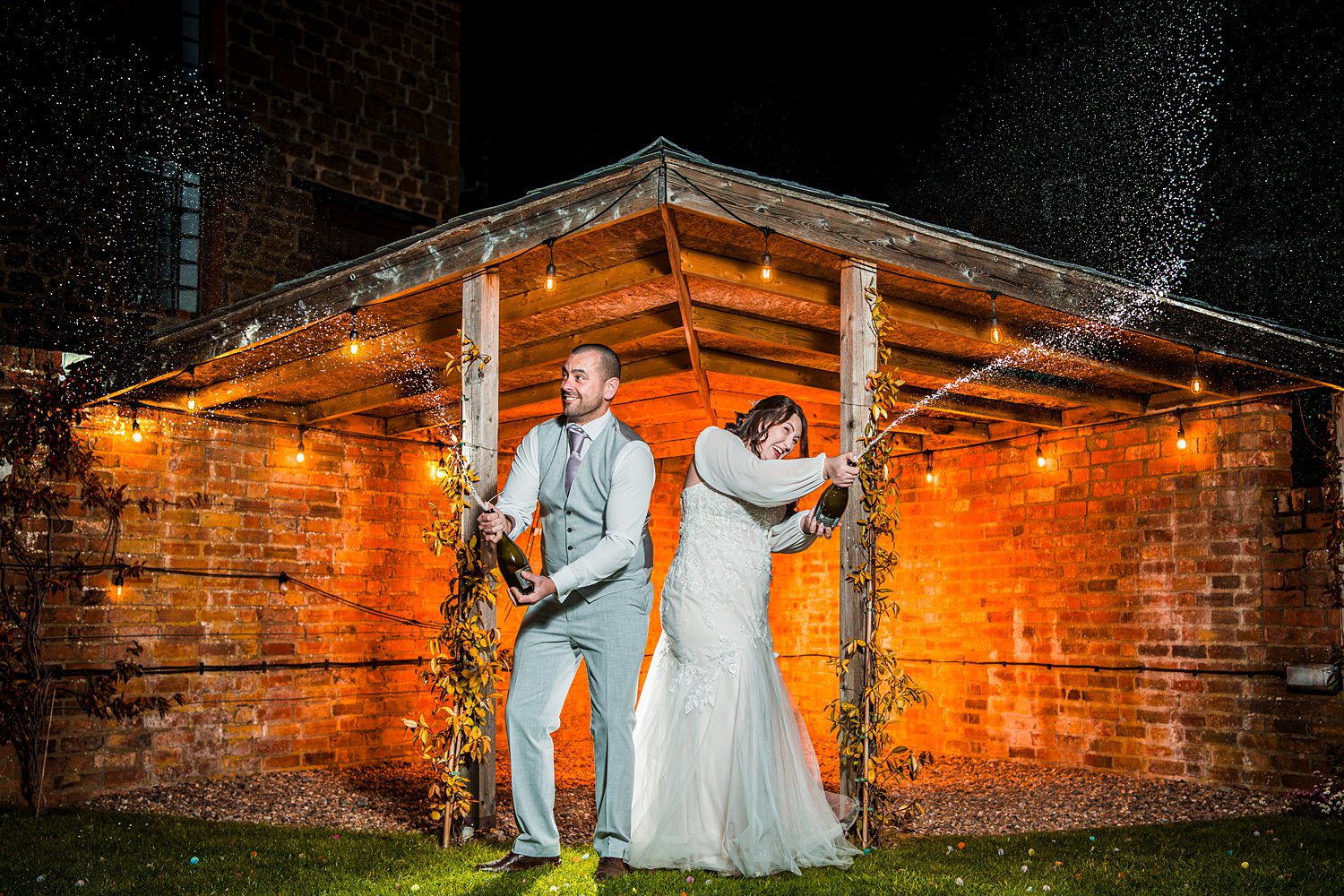 Couple celebrate with champagne under rustic shelter.